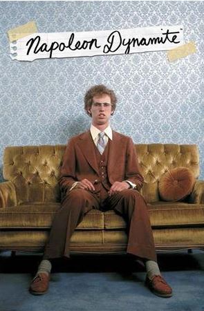 A man with curly hair and glasses sits on a mustard yellow couch, wearing a brown suit and tie. The background features light blue patterned wallpaper. Above him, text reads "Napoleon Dynamite" in a handwritten style on torn notebook paper. Ideal for any Movies & TV Collection, this hit movie poster from MTV is printed on premium 150gsm gloss paper.