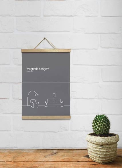A minimalist room features a poster of living room outlines hanging on a white brick wall, secured by the "Magnetic Timber Hanger 21.5cm Natural" from Blue Dog Posters. Below the poster is a green cactus in a beige, woven pot, adorning the classic look of the wooden floor.