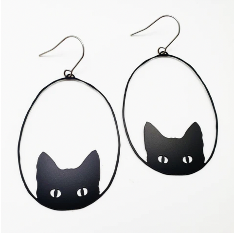 The Denz Cat Black Earrings by Blue Dog Posters are black cat-themed and handmade in Noosa. They showcase an outline of a cat’s head with pointed ears and white eyes on a simple, minimalist white background. Crafted from recycled stainless steel, these lightweight statement earrings are framed in oval wire hoops with hooks for wearing.