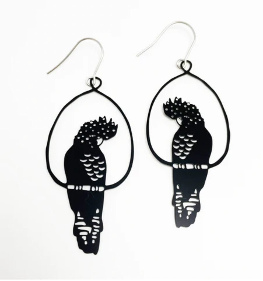 The Denz Cockatoo Black Earrings by Blue Dog Posters are a pair of handcrafted earrings from Noosa, shaped like birds perched in oval frames. Featuring intricate cutouts that highlight the details of the feathers and body, these super lightweight statement pieces are crafted from recycled stainless steel and come with simple fishhook wire closures.