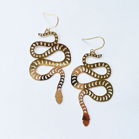 The Denz Snake Dangles Gold Earrings by Blue Dog Posters feature a pair of snake-shaped earrings with intricate cutout patterns, handcrafted in Noosa from recycled stainless steel. These lightweight statement earrings have fishhook backings and showcase the snake's body in a curvy, twisted design against a plain white background.