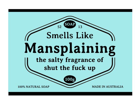 A blue soap label reads, "Hustle and Co Soap - Mansplaining. Smells Like Mansplaining. The salty fragrance of shut the fuck up." Infused with natural skincare ingredients, this 100g exfoliating soap by Blue Dog Posters is stamped with "100% NATURAL SOAP" at the bottom left and "MADE IN AUSTRALIA" at the bottom right.