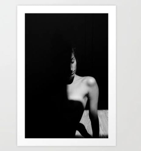 Turning to Dust by Astrid Arkhangelsky, available from Y, features a black and white photograph of a person with their eyes closed and upper body exposed, sitting partially in shadow. The strong contrast between light and dark emphasizes the contour of their shoulder and face. This Art Print is part of our Gallery Series, created on premium archival paper to ensure longevity.