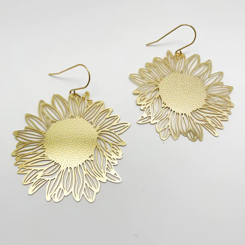 The Denz SunFlowers Gold Earrings by Blue Dog Posters are handmade in Noosa, featuring intricate petal details and a textured center. Crafted from recycled stainless steel, these lightweight statement earrings boast hook-style fastenings for easy wearing and are displayed against a white background.