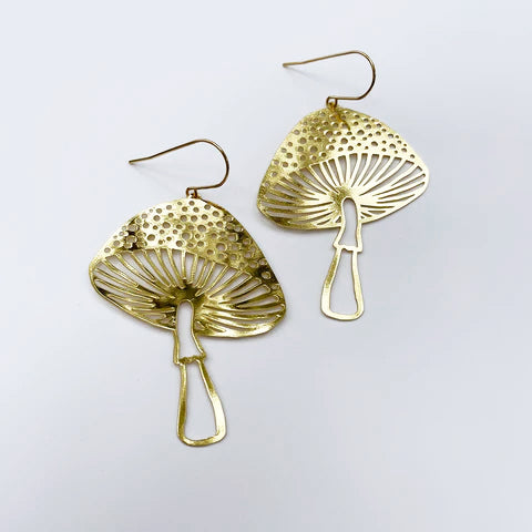 Displayed on a plain white background, the Denz Toadstools Gold Earrings by Blue Dog Posters are lightweight statement pieces shaped like mushrooms. They feature a gold-colored metal with intricate cut-out details, including detailed caps adorned with small holes and minimalist-style stems, and are complemented by comfortable surgical steel hooks.