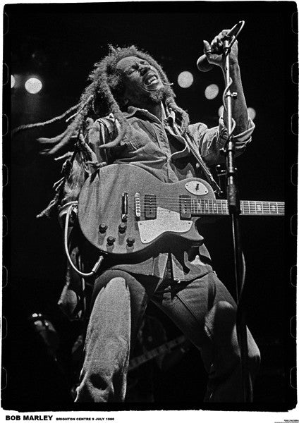 Black and white photo of a musician with dreadlocks passionately performing on stage with a guitar. The artist is leaning back, eyes closed, and singing into a microphone. Stage lights create a dramatic backdrop. Text at the bottom says "BOB MARLEY BRIGHTON CENTRE 3 JULY 1980.” BOB MARLEY BRIGHTON 1980 by MUS 310 available on premium 150gsm gloss paper for an elegant touch.