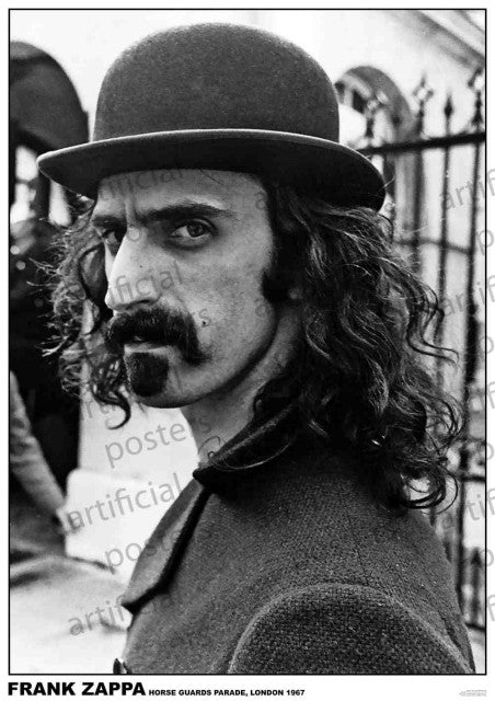 A striking black-and-white portrait captures Frank Zappa with his long curly hair, thick mustache, and goatee, dressed in a bowler hat and coat. He gazes intently at the camera while an outdoor scene with a wrought-iron gate and a building serves as the backdrop. The text reads "FRANK ZAPPA Horse Guards Parade, London 1967." This product, named "Frank Zappa Horse Guards Parade" by MUS 174, is perfect for any rock poster or collection.