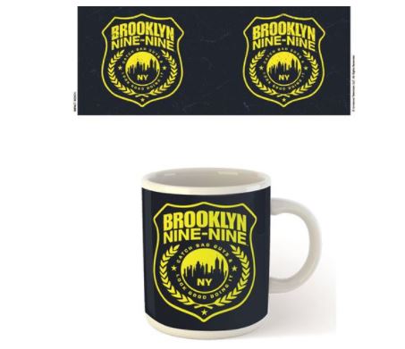The Brooklyn 99 Shield Mug by Blue Dog Posters, part of our Homewares Collection, showcases a white ceramic finish and features a black background adorned with the yellow and black Brooklyn Nine-Nine logo. The logo displays a police badge with "Brooklyn Nine-Nine," "NY," a city skyline, and laurel leaves. Above the mug are two digital images of the same logo.