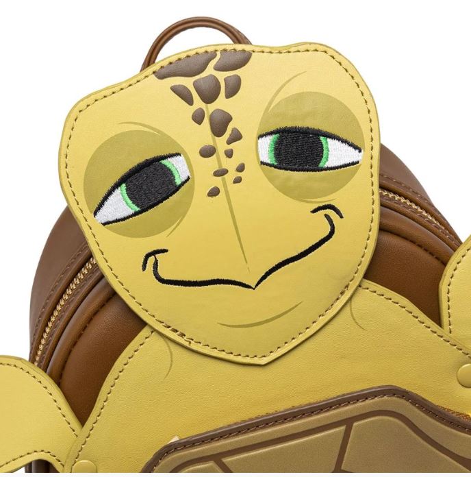Close-up of the Finding Nemo Crush Mini Backpack by Blue Dog Posters, featuring a brown and yellow faux leather design with a charming turtle motif. The top flap boasts a large, smiling turtle face with green eyes and brown spots on its head, perfectly capturing the likeness of Crush from Finding Nemo. Detailed stitching outlines the turtle's features impeccably.