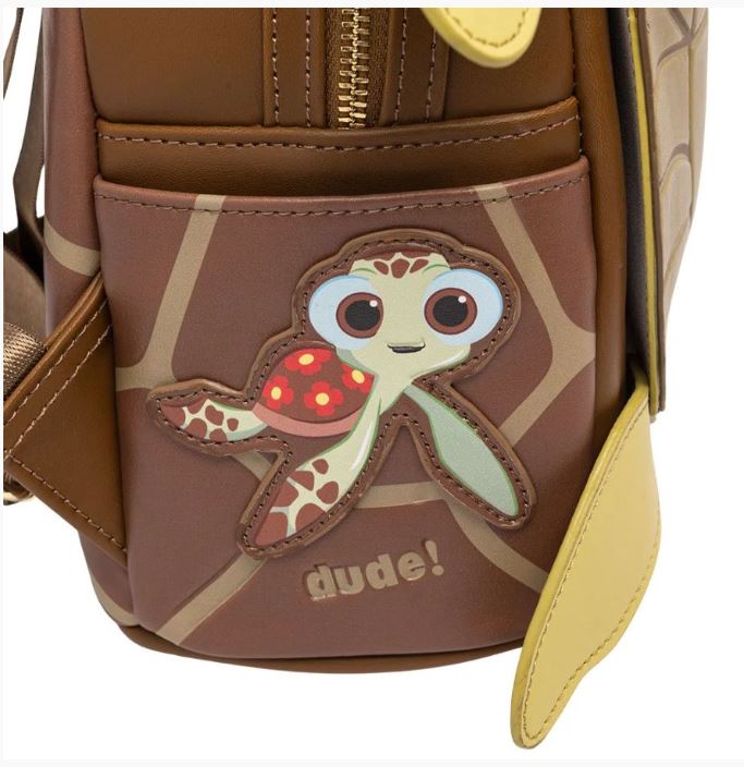 Introducing the Finding Nemo Crush Mini Backpack by Blue Dog Posters: This charming brown faux leather mini backpack showcases an adorable cartoon sea turtle with large eyes and colorful fins stitched onto the front pocket, along with the word "dude!" written below it. The backpack features light brown detailing and yellow zipper pulls—perfect for a Crush cosplay!