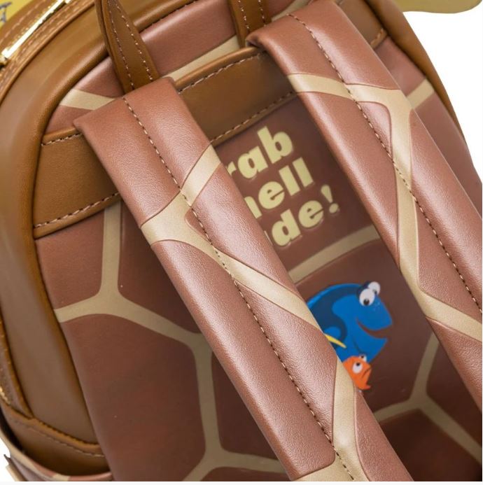Close-up image of the back of the Blue Dog Posters Finding Nemo Crush Mini Backpack, crafted in brown faux leather with tan straps and a turtle shell design. The text on the backpack reads "Grab shell dude!" accompanied by an illustration of two cartoon fish. Ideal for any Crush cosplay or Finding Nemo enthusiast!