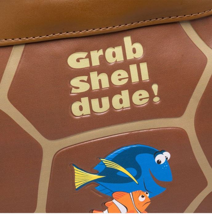 A close-up of the Finding Nemo Crush Mini Backpack by Blue Dog Posters, showcasing text that reads "grab shell dude!" in yellow letters. Below the text is an illustration of two fish, one blue and one orange with white stripes, from the animated movie Finding Nemo.