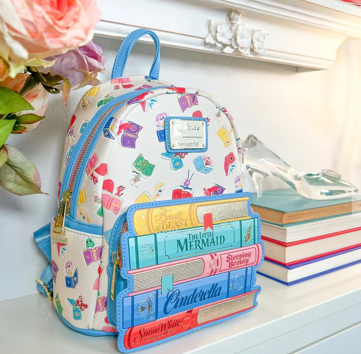 A Disney Princess Books Mini Backpack from Blue Dog Posters, featuring colorful designs of classic fairy tales like "The Little Mermaid," "Sleeping Beauty," "Cinderella," and "Snow White," sits on a white mantle next to a stack of books and a glass slipper. Flowers nearby add to the whimsical charm.