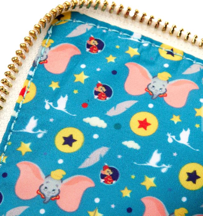 Close-up of the vegan leather Dumbo 1941 Book Convertible Crossbody by Blue Dog Posters, showcasing a whimsical pattern featuring flying Dumbo elephants, circus elements such as stars and balls, clouds, and colorful starbursts set against a light blue background. The fabric is bordered by a gold-colored zipper.