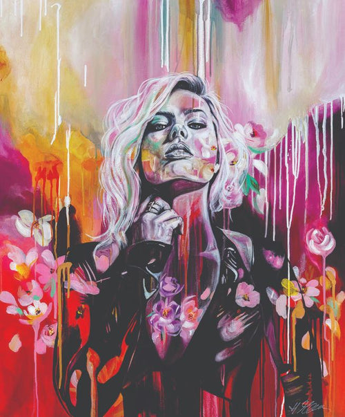Emergence by Heylie Morris, part of the Blue Dog Posters Artist Series Art Print collection, features a vibrant portrayal of a woman with flowing blonde hair wearing a black jacket. The background bursts with splashes of pink, orange, and purple, adorned with flowers and paint drips that intertwine around her figure to create a surreal effect.