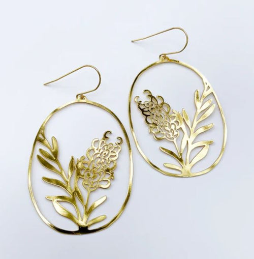 The Denz Grevilleas Gold Earrings by Blue Dog Posters feature an exquisite oval shape with intricate floral cutout designs, showcasing a flower and leaves. Made from recycled stainless steel, these lightweight statement earrings come with hooks for easy wear. Their delicate details are amplified against a plain white background, making them truly stunning accessories.