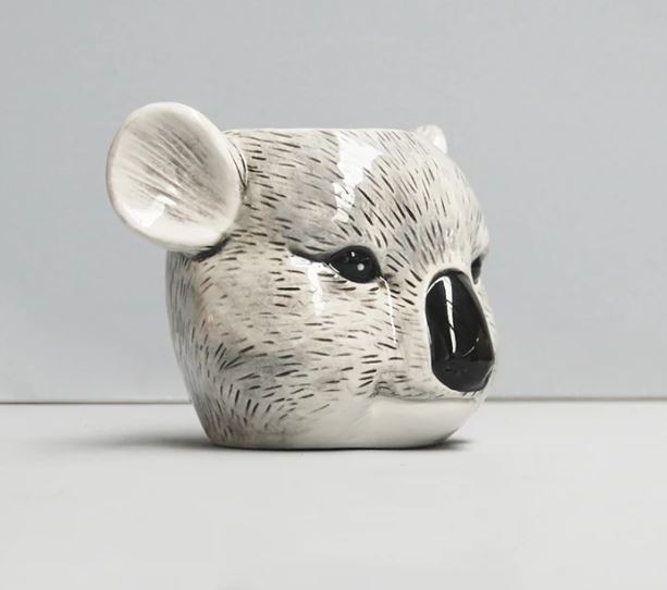 Introducing the Ceramic Planter - Koala by Blue Dog Posters, a charming ceramic mug designed to resemble a koala's head. It's perfect for sipping your favorite beverage or as an adorable decorative planter for succulents. The mug features detailed facial elements such as black eyes, a black nose, and large rounded ears. The textured surface mimics the koala's fur, showcasing shades of gray and white for added realism.