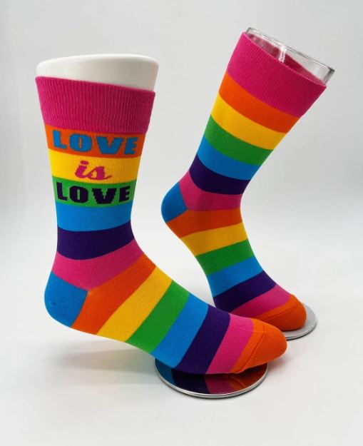 Two colorful men's crew socks from Blue Dog Posters feature horizontal rainbow stripes in vibrant colors. The Love is Love Socks display an inspirational "LOVE is LOVE" message in bold letters at the top. They are shown standing on clear circular stands against a plain white background.