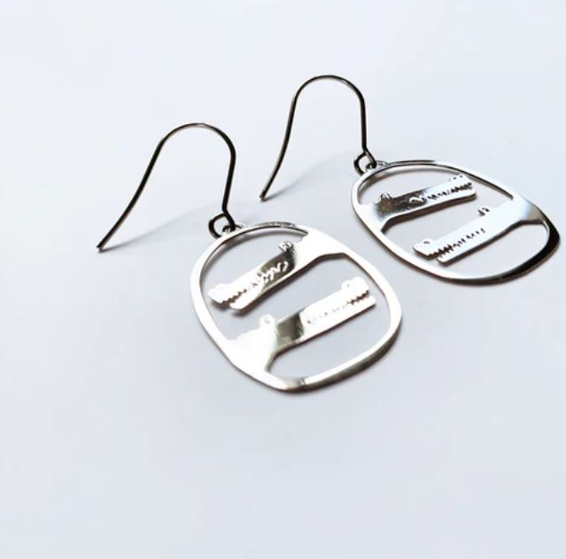 A pair of modern Denz Mini Earrings Crocs Silver from Blue Dog Posters, featuring silver surgical steel hooks. Each earring showcases an oval frame with cut-out designs that resemble abstract shapes and lines. Crafted from recycled plated stainless steel, these Australian-made earrings are displayed on a plain, light gray surface.
