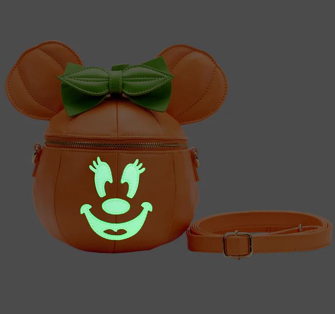 A round, orange handbag shaped like a pumpkin with mouse ears is shown. The Disney Minnie Pumpkin Face Crossbody Bag by Blue Dog Posters, complete with a green bow on top and glowing smile, makes for the perfect Halloween accessory. A detachable strap is placed next to this stylish bag.