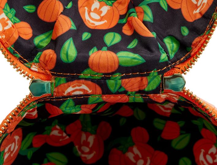 A close-up view of the inside of a Disney Minnie Pumpkin Face Crossbody Bag by Blue Dog Posters reveals a colorful, playful Halloween-themed lining adorned with smiling jack-o'-lanterns and green leaves on a black background. The bag features an orange zipper with green zipper pulls, making it the perfect Halloween accessory.