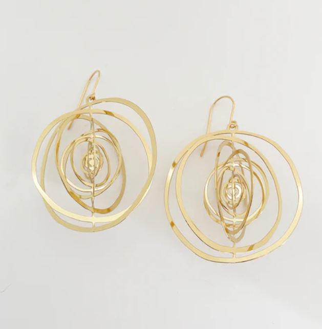 The Denz Orbit Dangles Gold Earrings by Blue Dog Posters feature a modern, artistic design with concentric hoops of varying sizes. Each lightweight earring boasts an intricate arrangement of rings, creating a visually striking and elegant appearance against a plain white background.