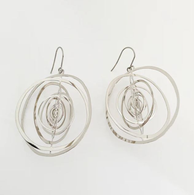The Denz Orbit Dangles Silver Earrings from Blue Dog Posters are a pair of sleek, silver spiral earrings made from recycled stainless steel. They feature a contemporary design with multiple interconnected circular loops and hang gracefully from simple hooks, offering the perfect accessory for any modern look. The background is plain white.