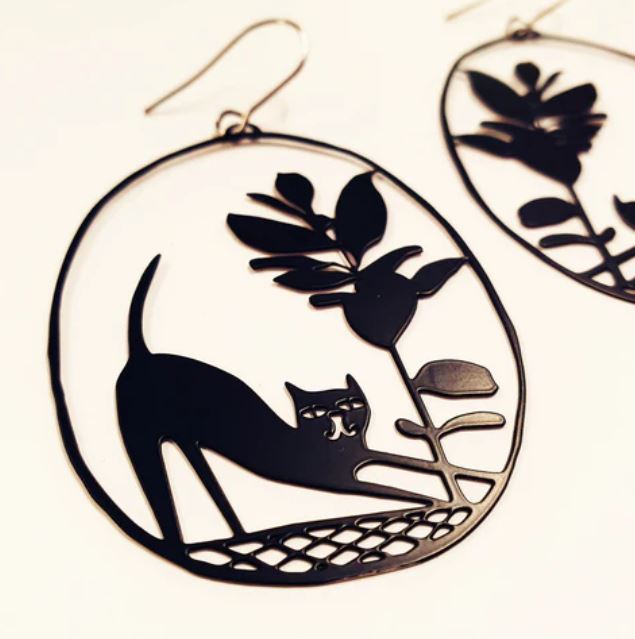 Introducing the Denz Pickles Cat Black Earrings from Blue Dog Posters: These oval-shaped statement earrings boast delicate black cut-out designs of a stretching cat and a flower. Intricately detailed, they beautifully capture the elongated form of the cat alongside the leaves and petals of the flower, all elegantly framed within a thin circular border made from recycled stainless steel.
