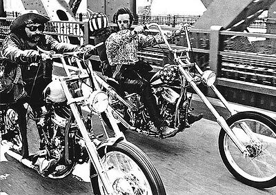 Two motorcycle riders are depicted riding chopper-style bikes side by side on a bridge. One rider sports a rugged look with a beard and sunglasses, while the other wears a star-spangled helmet, patterned shirt, and sunglasses. This scene could be straight out of the MTV 244 Easy Rider - Still Bikin Colour: Film Classics Poster.