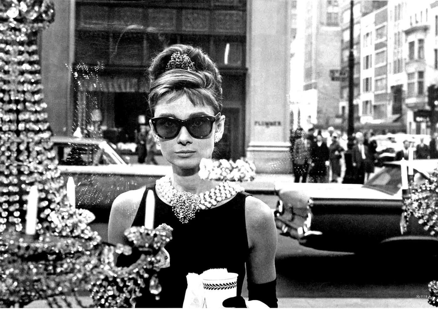A stylish woman in black and pearls stands on a city street, evoking iconic movie poster vibes. The 'Audrey Hepburn Breakfast at Tiffany's Black and White' by A3 is perfect as an A3 satin paper poster for chic display.