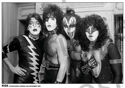The product "Kiss Hilton Hotel London 1982" by MUS 263 features a striking black and white photograph reminiscent of a classic rock poster. It captures the four band members of Kiss posing together, adorned in elaborate costumes and distinctive face paint. Their theatrical, rock-inspired outfits stand out against an interior setting with wood elements in the background.