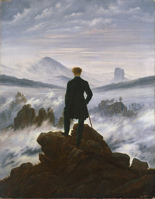 A man in a dark coat with a walking stick stands atop a rocky cliff, gazing over fog, in "Caspar David Friedrich - Wanderer," an evocative poster by Blue Dog Posters inspired by the iconic Romantic painting.