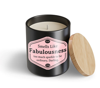 A black candle jar with a wooden lid from Blue Dog Posters, the Fabulousness Candle Hustle & Co, features a pink label that reads: "Smells Like Fabulousness—too much sparkle to be ordinary, Darling.