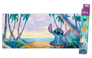 An illustration of Stitch, the blue alien-like character from Lilo & Stitch, sitting on a beach with palm trees and a sunset in the background. The character has large ears and black eyes. The scene is depicted on the Blue Dog Posters' "Lilo & Stitch - Stitch - XXL Gaming Mat," which features a wide, rectangular design with a non-slip base, perfect for smooth mouse control in your gaming room. Matching packaging stands beside it.
