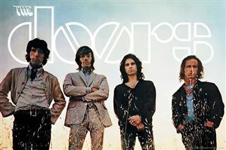 Four men pose before a large "The Doors - Waiting for the Sun" logo by MUS 183—two in dark jackets, one in a striped suit, and one in a patterned shirt—all facing the camera against a pale sky.