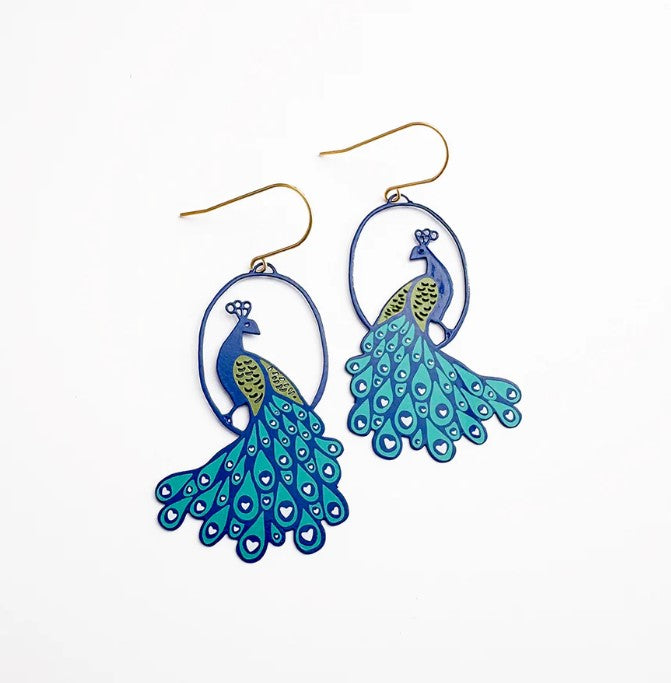 Peacock Earrings by Denz from Blue Dog Posters feature hand-drawn blue and green details, long feathered tails, and gold hooks, shown on a white background.