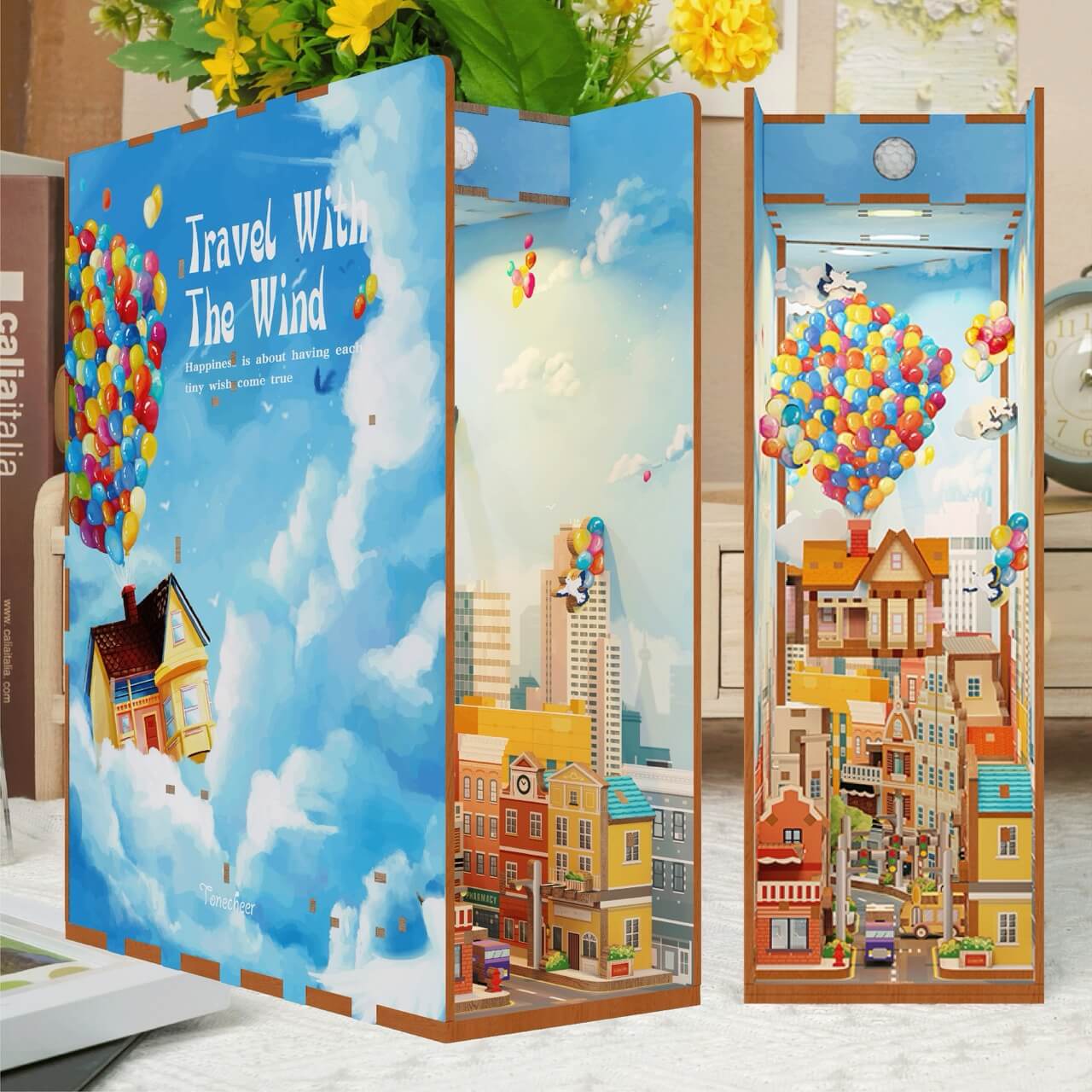 The Travel With the Wind Book Nook Tonecheer by Blue Dog Posters features vibrant city streets, houses, and rainbow balloons inspired by "Up," with a cover saying "Travel With The Wind" set against a blue sky with clouds.