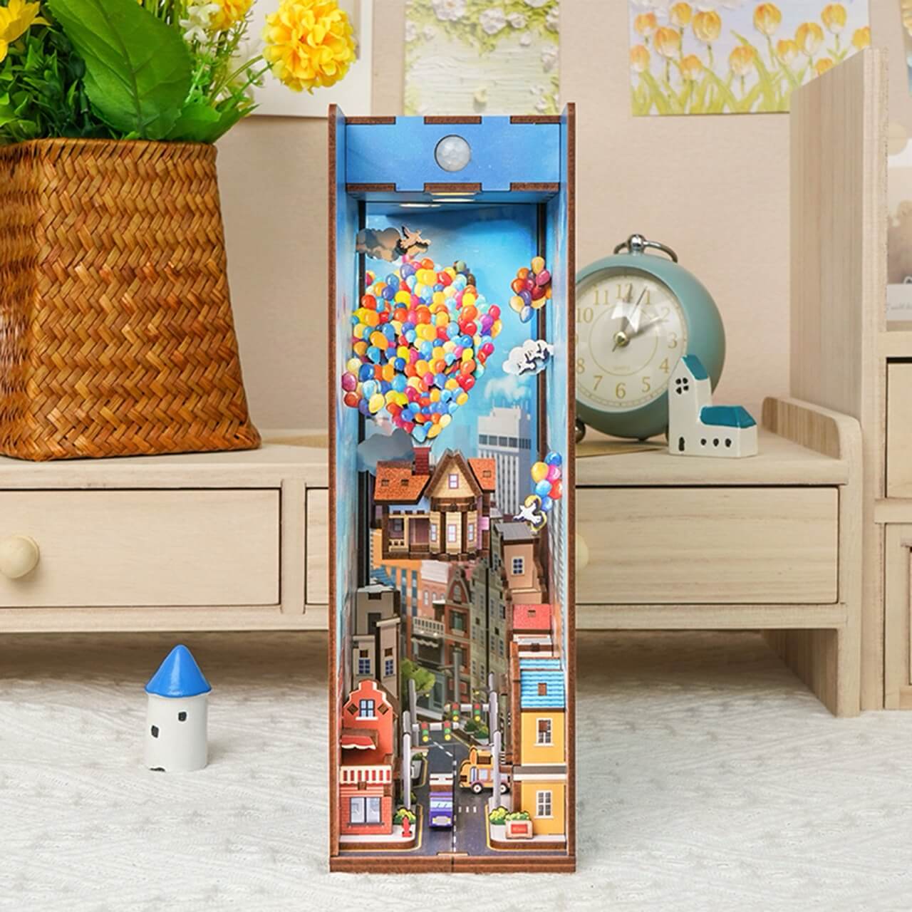 The Travel With the Wind Book Nook Tonecheer by Blue Dog Posters is a decorative wooden diorama with colorful houses and rainbow balloons, ideal as a whimsical book nook on a light table near your clock or wicker basket.