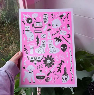 A hand is holding a vibrant "Flash Sheet A3 Risograph - Amy Hastings" poster from Blue Dog Posters against a window. The poster features a pink background adorned with various black-and-white doodles, including cats, skulls, flowers, eyes, and mystical symbols. Plants and a view of the outdoors can be seen in the background.