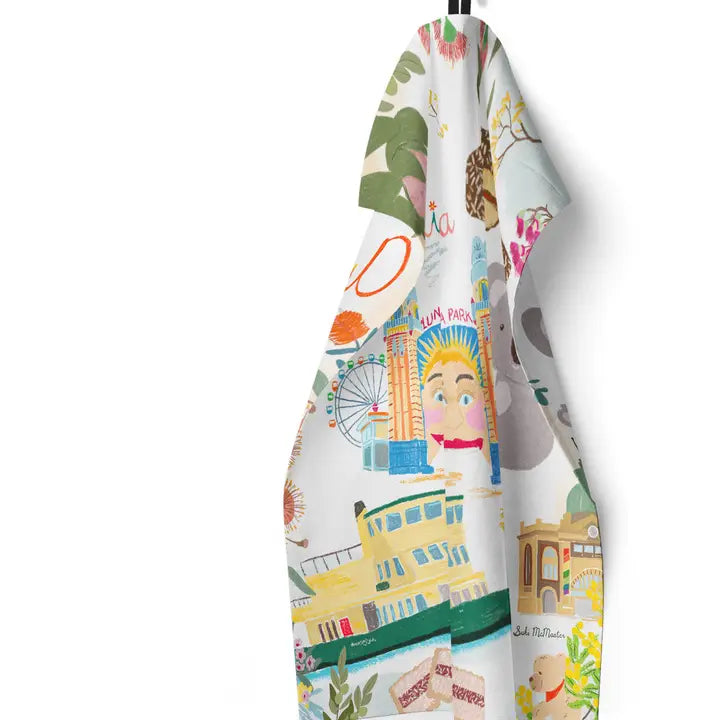 The Australiana Kitchen Tea Towel by Blue Dog Posters features illustrated landmarks, Australian icons, and foods—like a ferris wheel, smiling face, buildings, and vibrant plants—bringing a lively cityscape theme to your kitchen.