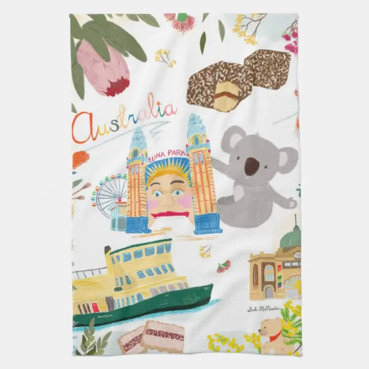 The Australiana Kitchen Tea Towel by Blue Dog Posters showcases a colorful Suki McMaster illustration of Aussie icons—koala, lamingtons, fairy bread, ferry, Luna Park entrance, ferris wheel, and native flowers with "Australia" in playful script.
