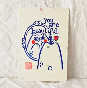Bear gazes into a mirror with "you are beautiful" above and a red heart nearby. Bear's cheeks are painted red in this original lino print design by Misu-Juju, available as the Bear Beautiful Small Lino Print from Blue Dog Posters.