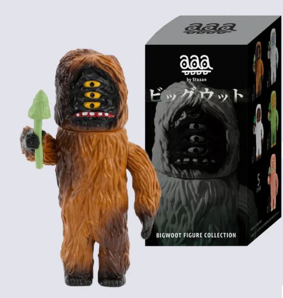 A brown, furry, four-eyed monster inspired by folklore holds a green tree beside its black box with Japanese text. The box reads "BigWoot Figure Blind Box" by Blue Dog Posters.
