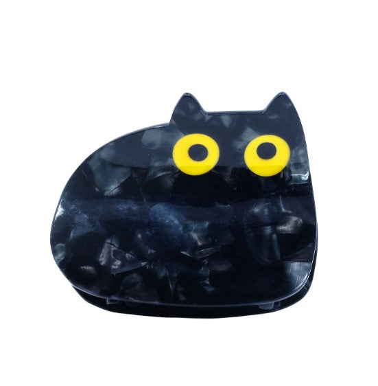 The Void Black Cat Hair Claw by Blue Dog Posters features a unique black cat shape with pointed ears and large yellow eyes, perfect for lovers of quirky accessories. Photographed against a white background.