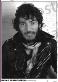 A man with curly hair and a beard smiles slightly while wearing a leather jacket and scarf in this vintage-style black and white MUS 069 poster: "BRUCE SPRINGSTEEN - RAI Amsterdam 1975." Perfect for any music collection.