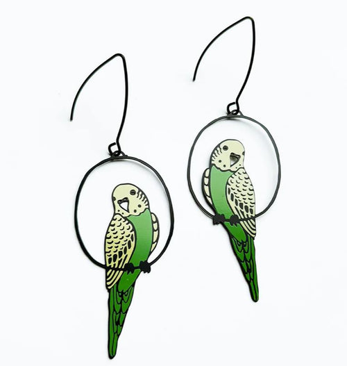 Blue Dog Posters' Budgie Black Green Yellow Denz Earrings feature lightweight green and yellow parakeet shapes perched on black wire hoops, shown against a white background.