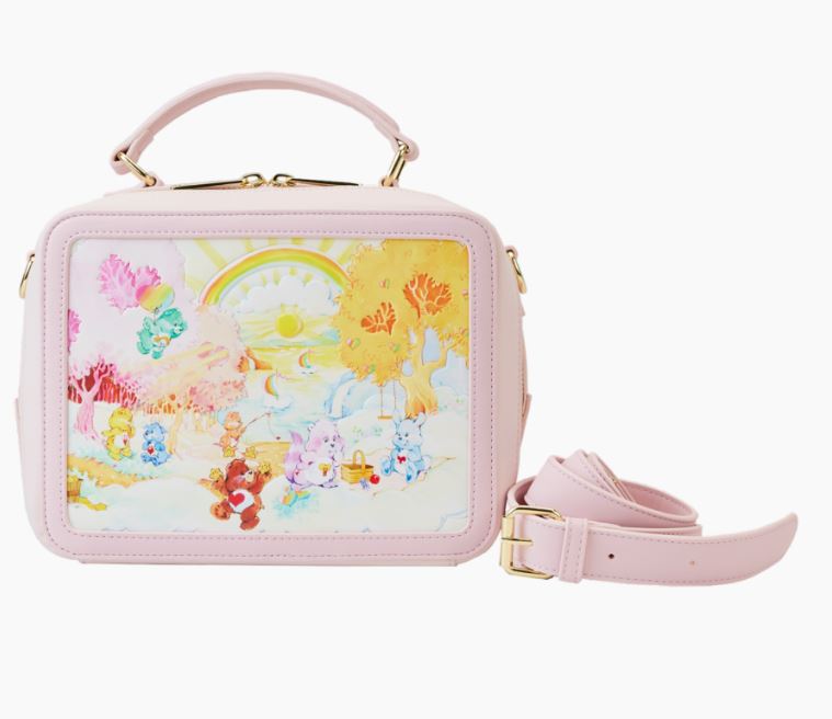 The Care Bears & Cousins Lunchbox Crossbody by Blue Dog Posters is a small, pastel pink handbag crafted from vegan leather, complete with a detachable strap. It showcases a vibrant and playful illustration of cartoon animals in a sunny autumn landscape featuring trees and a rainbow. The bag includes gold hardware and features both a top handle for convenient carrying.