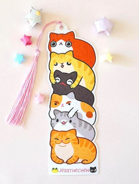 The Bookmark Cat Stack by Jess Chen from Blue Dog Posters features five colorful cartoon cats, a pink tassel, pastel origami stars, and "Jessthechen" written at the bottom for a cute touch.