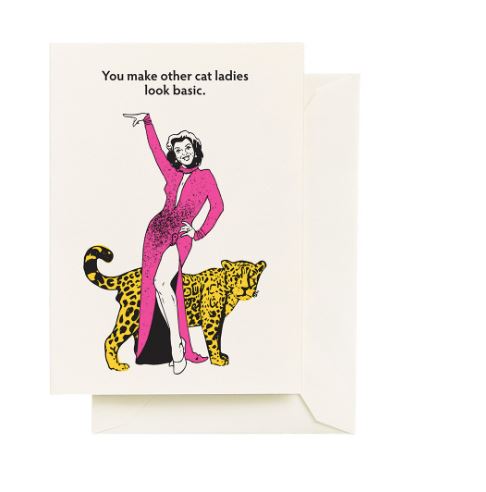 The Cat Ladies Greeting Card by Blue Dog Posters features a confident woman in a pink dress with a leopard. Printed on recycled paper with "You make other cat ladies look basic." Blank inside, envelope included. Eco-friendly.