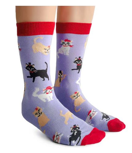 A pair of feet wearing Blue Dog Posters’ Cats in Hats Socks—purple women’s socks with playful cartoon cats in various colors and hats, featuring red heels, toes, and cuffs.